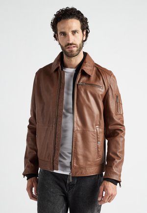 Brun læderjakke med lynlås foran, to sidelommer og en lynlåslomme på armen. Har et quiltet mønster på skuldrene.