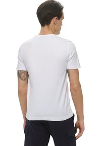 T-shirt bianco in cotone con maniche corte, colletto a giro standard e una texture liscia, indossato da una persona vista di spalle.