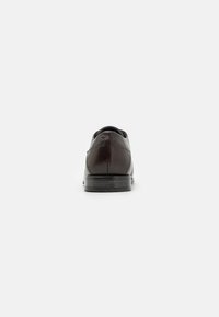 Chaussure en cuir marron avec un bout arrondi, texture lisse, couture minimale et semelle en caoutchouc noir. Vue de l'arrière.