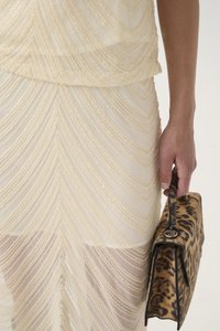 Leopardmønstret håndtaske med en struktureret form og flad hank, parret med et beige outfit med vertikale, perlebesatte, scalloped mønstre.