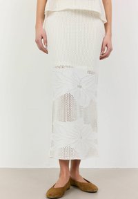 Fustă tricotată albă cu un model floral, textură ondulată și lungime până la jumătatea gambei. Asortată cu balerini maro, evidențiind un stil lejer.