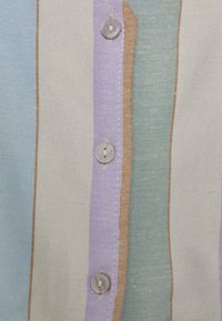 Tessuto a righe multiple con tonalità di blu, lilla, verde e beige. Presenta bottoni trasparenti e cuciture visibili lungo le cuciture.