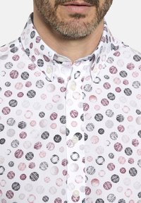 Weißes Hemd mit Knöpfen und einem gepunkteten Muster in verschiedenen Rosa-, Schwarz- und Grautönen. Verfügt über einen klassischen Kragen und subtile Texturdetails.