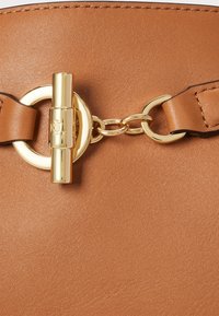 Torebka skórzana w kolorze brązowym z okrągłym, złotym detalem oraz łańcuszkowym akcentem. Gładka faktura z bezpiecznym mechanizmem zapięcia.