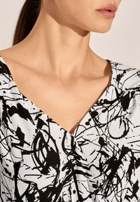 Schwarz-weißes Kleid mit V-Ausschnittdesign, das ein abstraktes Fleckenmuster aufweist. Glatte Stofftextur mit figurbetonter Silhouette.