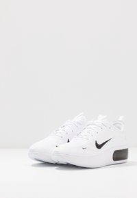 Vita sportskor med en texturerad ovandel, svart Nike swoosh och en formad häl. Har rundad tå och en dämpad sula.