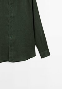 Chemise verte foncée à boutons avec un tissu texturé, manches longues et ourlet arrondi. Comprend des boutons assortis et un col classique.