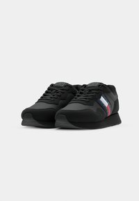 Schwarze Sportschuhe mit strukturiertem Obermaterial, ausgestattet mit einer stabilen Sohle und dekorativen Streifen in Blau, Weiß und Rot an der Seite.