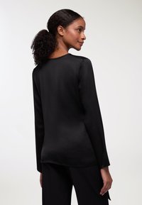 Maglia nera a maniche lunghe in un tessuto morbido e leggero, con scollatura rotonda e vestibilità rilassata. Design del fondo semplice e lineare.