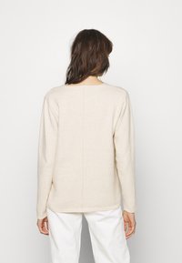 Maglione lavorato a maglia color crema con maniche lunghe, colletto rotondo e sottile dettaglio cucitura sul retro; abbinato a pantaloni bianchi. Tessuto morbido, peso medio.