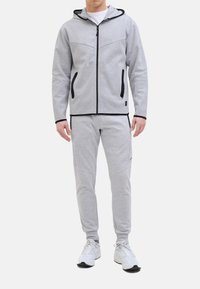 Grauer Reißverschluss-Hoodie mit Kapuze, schwarzen Akzenten und seitlichen Taschen, kombiniert mit passenden grauen Jogginghosen mit schmaler Passform und dezenter Logodetail.