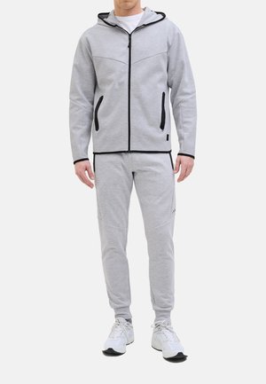 Grå zip-op hoodie med hætte, sorte detaljer og sidelommer, parret med matchende grå joggers med en tætsiddende pasform og diskret logo.
