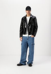 Sorte blanke læder bikerjakke med klapkerner, hvid t-shirt med rund hals, løse blå denim cargo bukser, sorte flade sko og en sort kasket.