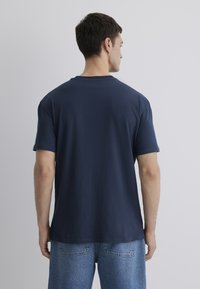 Marineblaue Baumwoll-T-Shirt mit kurzen Ärmeln, Rundhals-Ausschnitt und lockerem Schnitt. Sichtbare Nähte entlang des Saums und der Ärmeln.