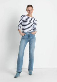 Gestreiftes Langarmhemd in Weiß und Marineblau, kombiniert mit hochtaillierten hellblauen Jeans und hellblauen Absatzstiefeletten.