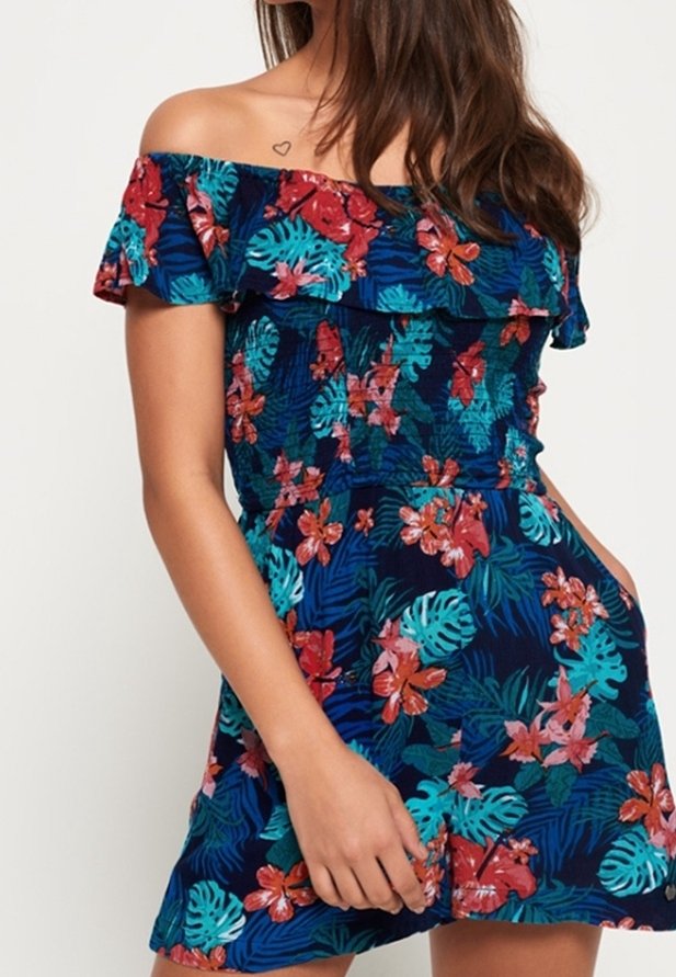 Bloemenprint off-shoulder jumpsuit in donkerblauw met tropische patronen in rood, turquoise en groen. Heeft een geruite halslijn en zakken.