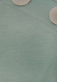 Tejido verde claro con punto texturizado; presenta dos grandes botones lisos de color crema en el lado derecho.