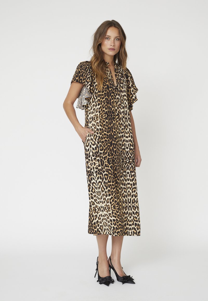 Rochie cu imprimeu de leopard, cu mâneci scurte bufante, decolteu în V și buzunare laterale. Materialul are o textură lucioasă. Pantofi cu toc stiletto negri, cu fundițe.