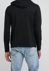 Svart långärmad hoodie med huva och avslappnad passform, tillsammans med ljusblå denimjeans med en klassisk femficksdesign.