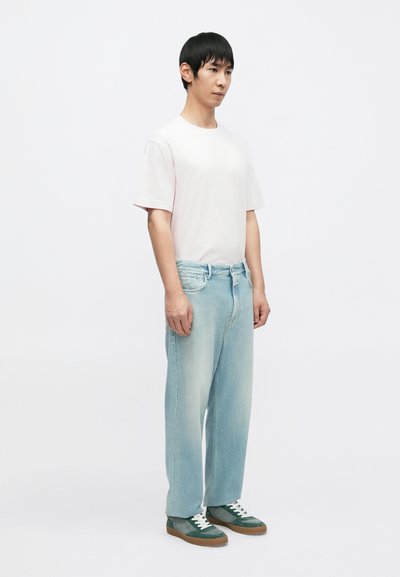 Ανοιχτό ροζ κοντομάνικη μπλούζα, ανοιχτό μπλε άνετο τζιν και πράσινο-μπλε αθλητικά παπούτσια με άσπρες κορδέλες σε ουδέτερο φόντο.