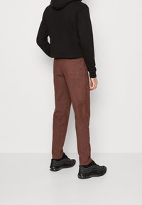 Brązowe spodnie z korduroju z bocznymi i tylnymi kieszeniami, o slim fit i tkanym wzorze, zestawione z czarnymi trampkami i czarną bluzą z kapturem.