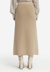 Beige stickad midikjol med ribbad textur, hög midja och rak silhuett, matchad med knähöga krämfärgade klackstövlar.