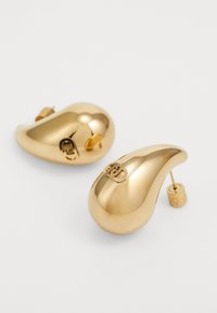 Orecchini color oro con un design liscio e curvo, caratterizzati da un perno sporgente e una piccola chiusura rotonda. Accentuati da un dettaglio con logo.