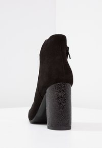 Czarny zamszowy botek za kostkę z błyszczącym, fakturowanym obcasem w kształcie bloku. Posiada zamek błyskawiczny po boku. Gładka powierzchnia o matowym wykończeniu.