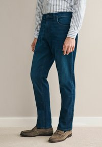 Donkerblauwe denim jeans met een rechte pijp, voorzien van voorzakken en een knoopsluiting. Draag een lichtgekleurde, gestreepte blouse met lange mouwen.