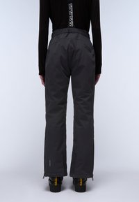 Zwarte, waterdichte sneeuwbroek met een relaxte pasvorm, elastische tailleband, ritszakken aan de zijkant en versterkte boorden, gecombineerd met zwarte laarzen.