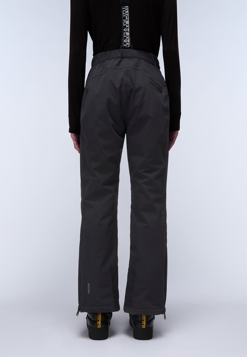 Pantalones de nieve impermeables y negros con un ajuste relajado, cintura elástica, bolsillos laterales con cremallera y puños reforzados, combinados con botas negras.