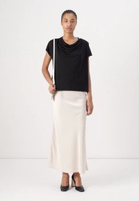 Top corto nero drappeggiato con maniche corte abbinato a una gonna in satin crema lunga fino al pavimento e scarpe con punta nera. Design semplice, texture liscia.