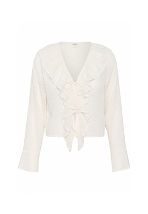 Blouse blanche raccourcie en tissu texturé avec un col à volants et un nœud à l'avant, dotée de manches longues qui s'évasent légèrement aux poignets.
