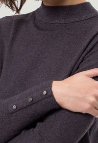 Pull à col roulé gris foncé avec texture côtelée et boutons décoratifs aux poignets. Matière douce et coupe ajustée.