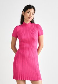 Tät rosa ribbad klänning med hög krage och korta ärmar, med vertikala veck som tillför textur och rörelse.