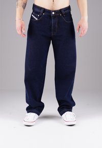 Dunkelblaue Denim-Jeans mit lockerer Passform, ausgestattet mit fünf Taschen, sichtbaren Nähten und einem klassischen Knopf- und Reißverschluss.