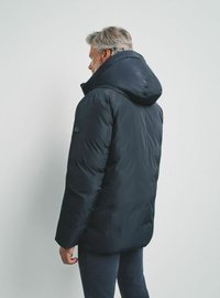 Granatowa kurtka puchowa z dużym kapturem, pikowanym wzorem i bocznymi kieszeniami. Kurtka ma luźny krój i miękkie wykończenie.