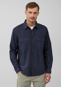 Marineblauw overhemd met lange mouwen, voorzien van twee borstzakken, knoopsluiting en een gladde katoenen textuur. Staande kraag en knoopmanchetten.
