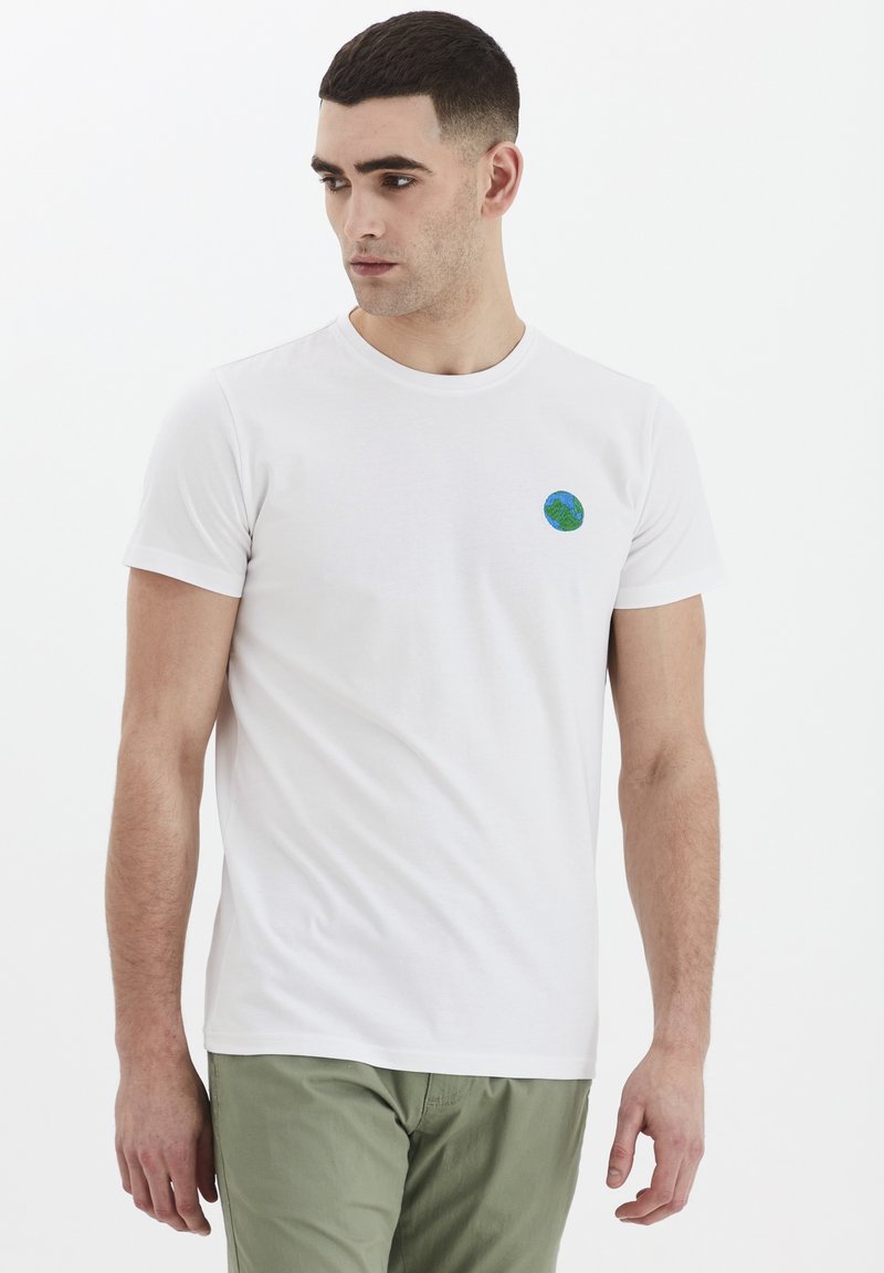 T-shirt bianca in cotone con un grafico circolare di un globo verde e blu sul petto. Collo a giro e maniche corte aderenti.