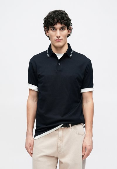 Μπλε ναυτικό πόλο με λευκό γιακά και λεπτομέρειες στα μανίκια, κατασκευασμένο από βαμβάκι, με τρυπητή τριάδα κουμπιών και άνετη εφαρμογή.