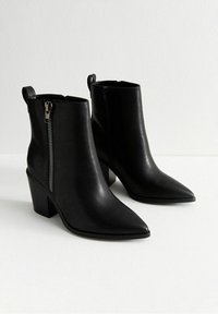 Botas de tobillo de cuero negro con puntas afiladas, cremalleras laterales y tacones gruesos. Diseño elegante con un acabado mate y hardware minimalista.