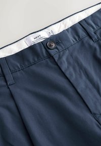 Granatowe spodnie o zwężanym kroju z zapięciem na guzik i wewnętrzną białą taśmą z napisem "NEXT Regular Tapered Fit".