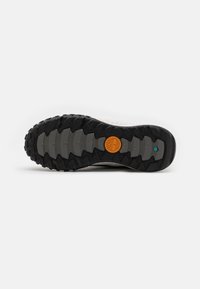 Suela de zapato con profundas estrías, exterior de goma negra, material de amortiguación gris y un logo circular naranja en el centro.