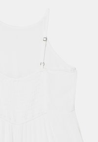 White dress featuring thin adjustable straps, textured bodice with gathered detailing, and a flowing skirt. Fabric appears lightweight.