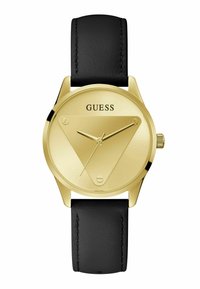 Montre analogique dorée avec un cadran en forme de triangle, bracelet en cuir noir, et la marque "GUESS" affichée en haut. Aiguilles des heures et des minutes simples.