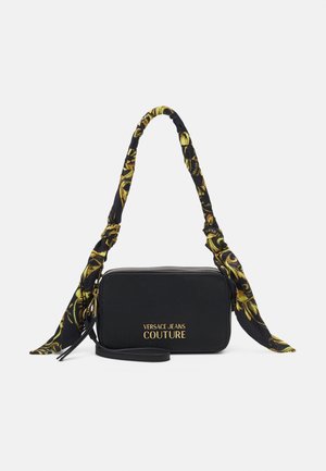 Zwarte rechthoekige schoudertas van Versace Jeans Couture met gouden logo, ritssluiting en een zwart-gele stoffen handgreep met patroon.