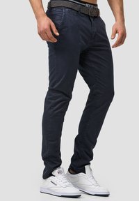 Navy blue chinos with a slim-fit design, featuring a textured waistband. Worn with white sneakers, highlighting the contrast in colors.
