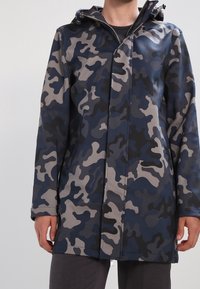 Vodeodolný kabát s maskáčovým vzorem v tmavě modré, šedé a černé barvě. Má kapuci, zapínání na zip a rovný střih.