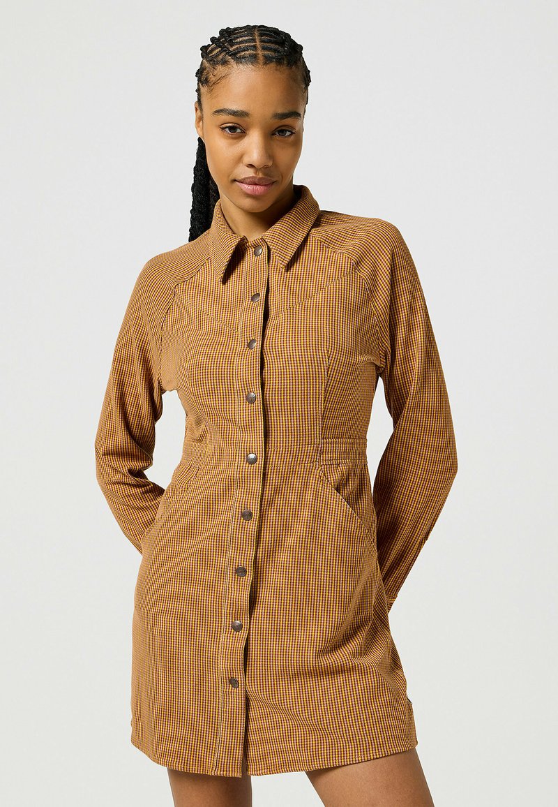 Abito a camicia con motivo a quadri nei toni del marrone e del giallo. Ha maniche lunghe, colletto e tasche laterali.