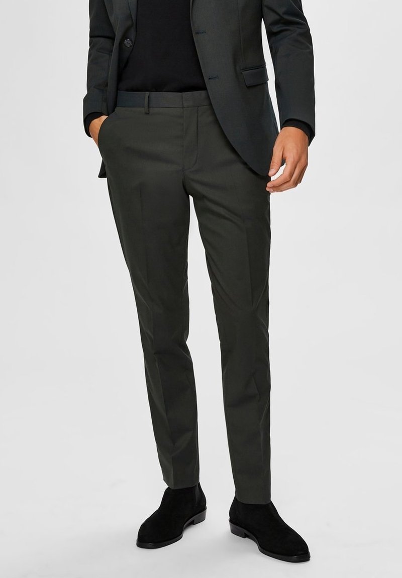 Dark green tailored trousers made of lightweight fabric, featuring a slim fit and a smooth texture, paired with black suede ankle boots.